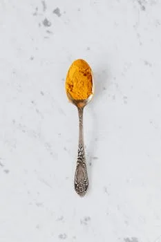 Top view of metal spoon with dry curcuma powder used for healthy gourmet food preparing placed on marble surface